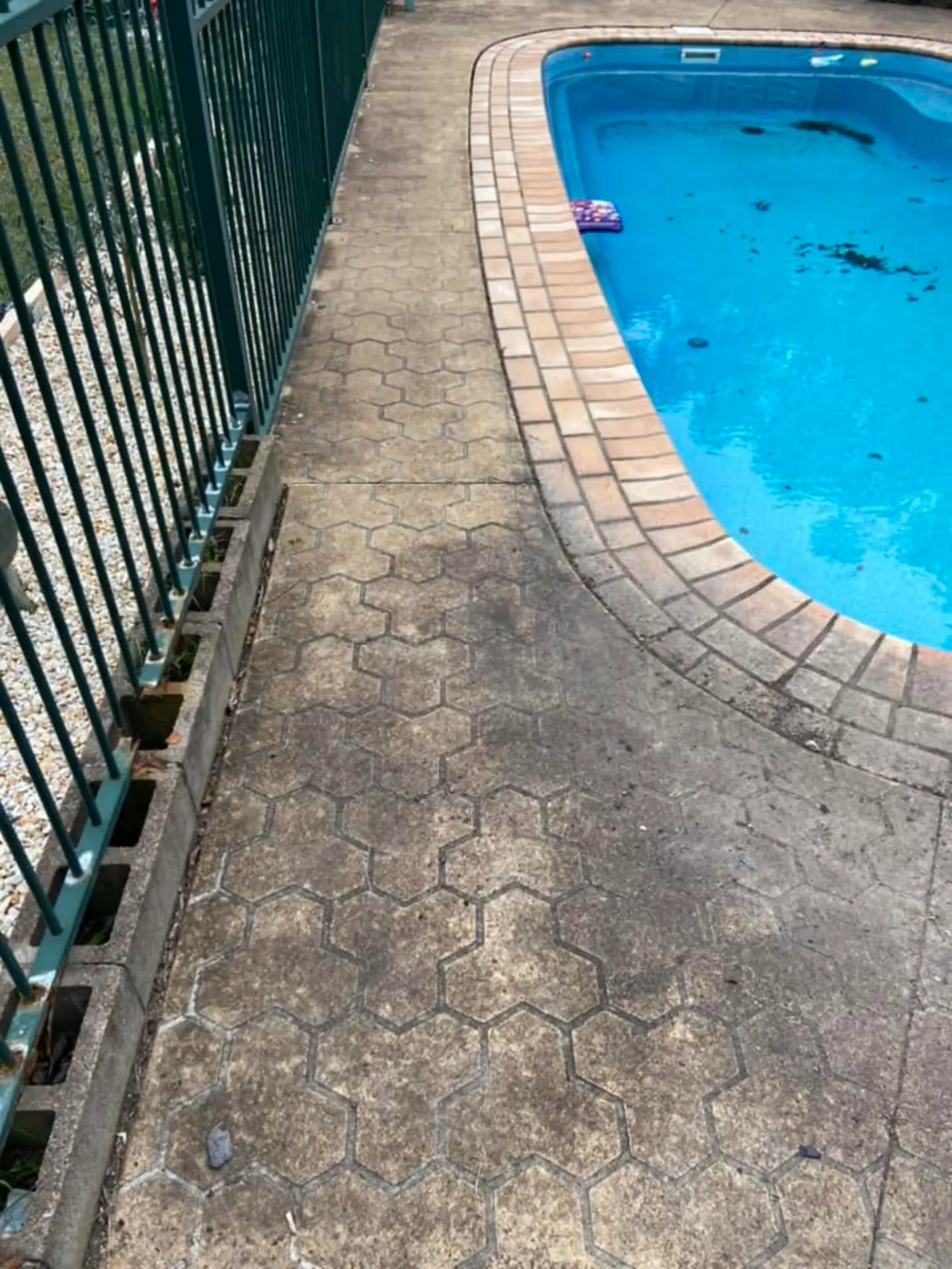 Hexagonal pool surround pavers before cleaning, darkened with dirt and algae