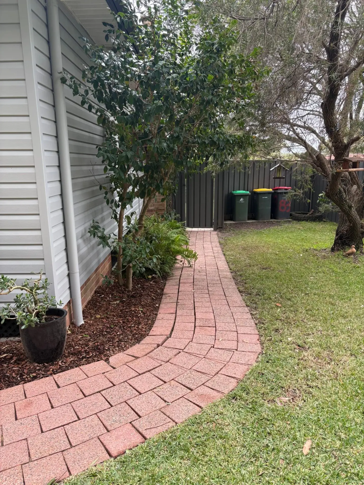Curved red brick garden path running alongside a home, ready for pressure cleaning